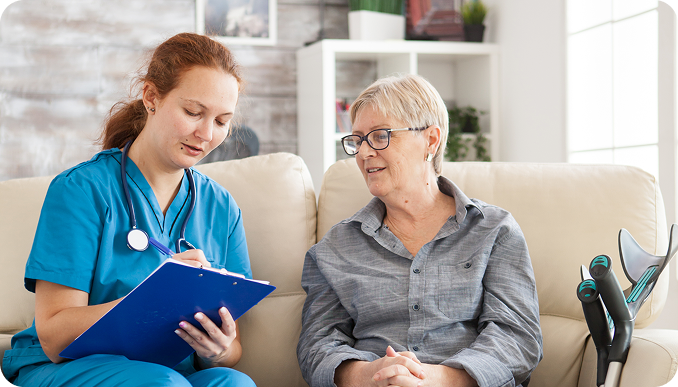 female-doctor-with-senior-woman-sitting-couch-nursing-home-writing-prescription-clipboard